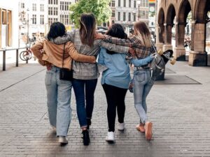 four friends walking in a city with their backs to the camera and arms around each other.