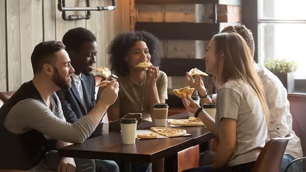 a group of friends smiling while eating pizza together in a restaurant